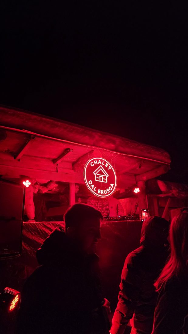 L'insegna al neon dello Chalet dal Bruscà accesa sopra la folla